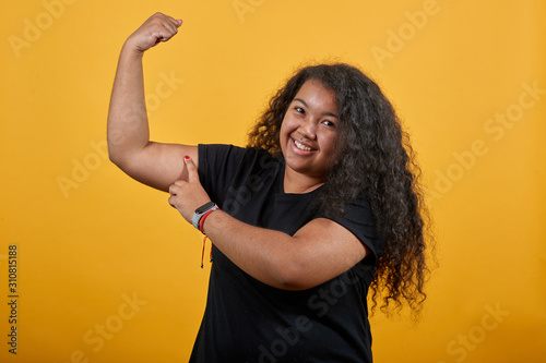 Attractive afro-american with overweight woman showing muscules, pointing finger on it, smiling over isolated orange background wearing fashion black shirt. People lifestyle concepte.