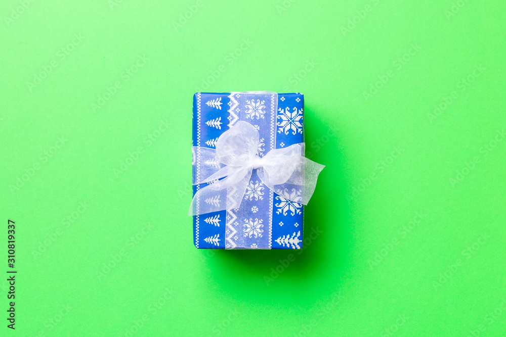 wrapped Christmas or other holiday handmade present in paper with white ribbon on green background. Present box, decoration of gift on colored table, top view with copy space.