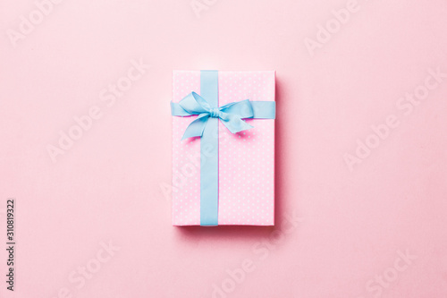 Gift box with blue bow for Christmas or New Year day on pink background, top view with copy space