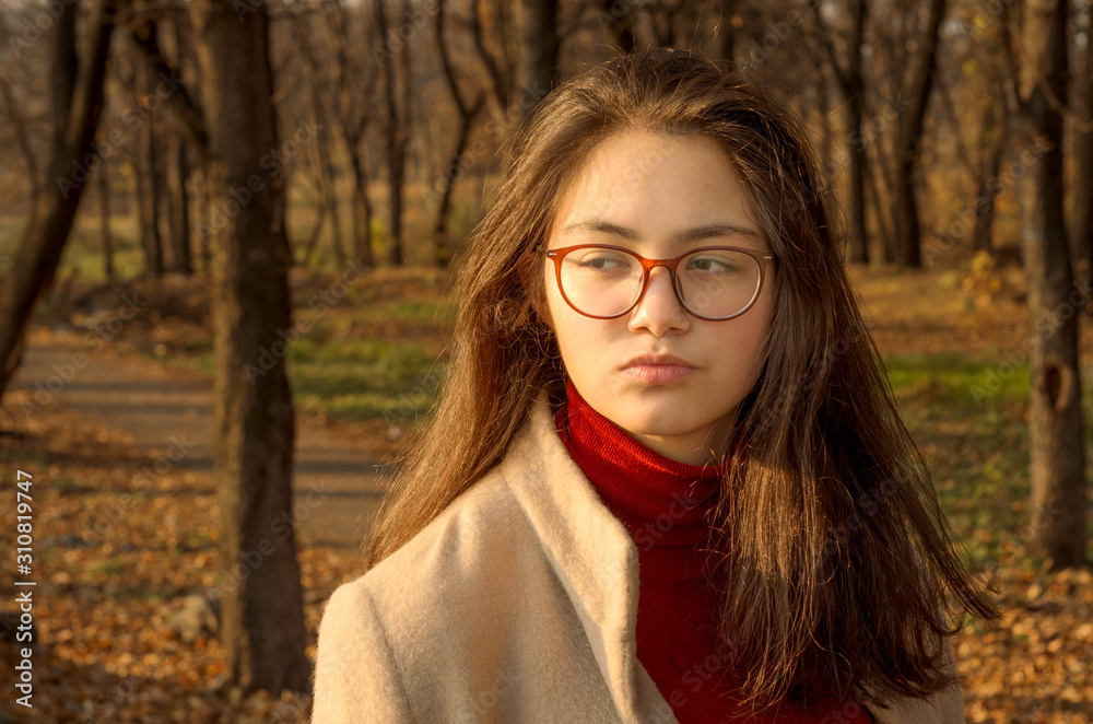 A young girl in a light coat and Burgundy turtleneck on a walk in the Park. Close up. Selective focus. A young girl in a light coat and Burgundy turtleneck on a walk in the Park. Close up. Selective focus.