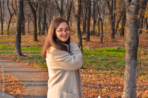 A girl in a light coat and glasses walks through the autumn Park with a book in her hands. The inscription on the book William Shakespeare. Soft focus.