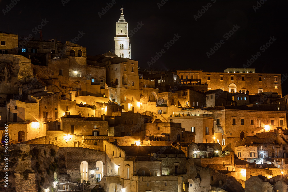 Beautiful night view of a street in the ancient stone city center of Matera, with the tower cathedral illuminated in the background.Basilicata. Italy