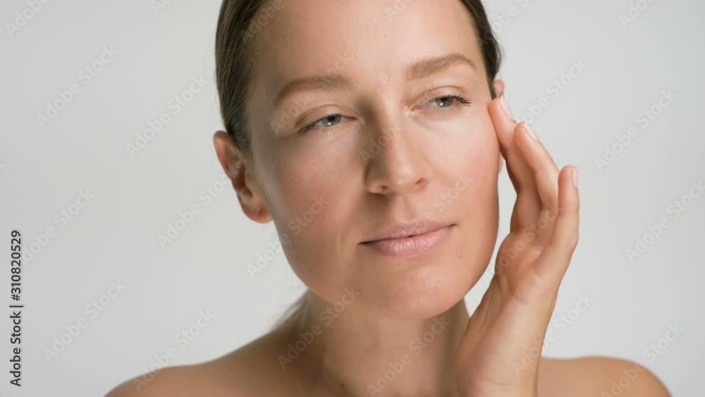 Close-up beauty portrait of young woman with smooth healthy skin, she gently touches her face with her fingers on white background and smiles Close-up beauty portrait of young woman with smooth healthy skin, she gently touches her face with her fingers on white background and smiles