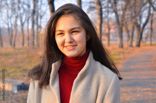 A young girl in a light coat and Burgundy turtleneck on a walk in the Park. Close up. Selective focus.