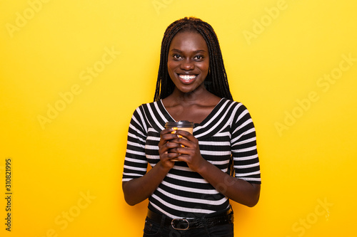 African American woman holds takeaway coffee on yellow background