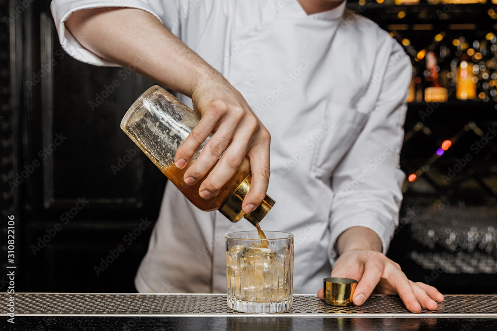 Bartender pouring a drink from a shaker into a rocks glass.