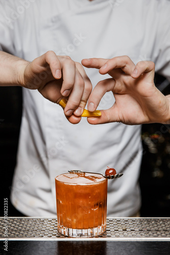 Bartender prepairing a cocktail at the bar, squeezing a lemon peel over a drink in a rocks glass