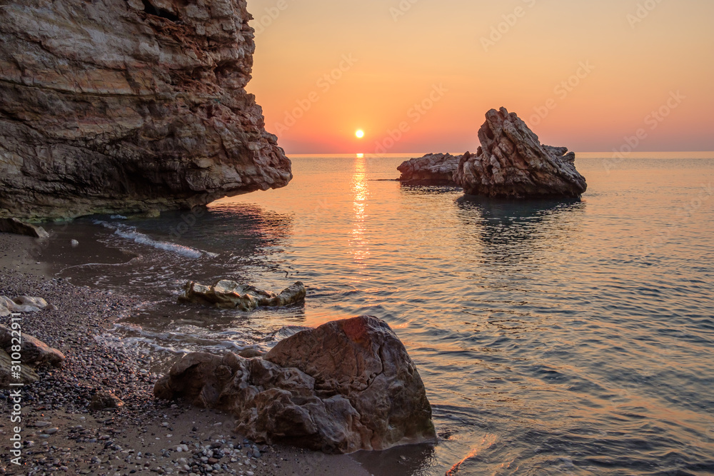 the sun rising over the sea in the early morning rocks and stones in the water a Sunny path