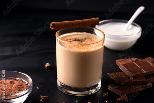lassi indian chocolate drink on a black background next to the ingredients with yogurt, cocoa and chocolate