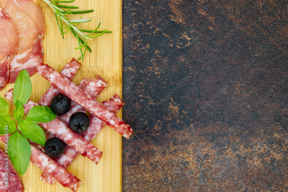 Obraz premium Meat and cheese plate antipasti snack with Prosciutto ham, Parmesan, Blue cheese, Cantaloupe melon and Olives on olive wood serving board on dark stone background