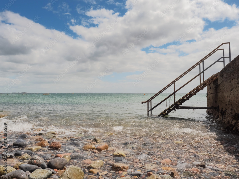 Fototapeta premium Blue ocean water and cloudy sky, Old metal stairs from a pier. Nature background.
