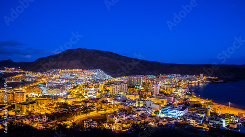 Spain, Tenerife, Los christianos city by night, aerial view above the houses and skyscrapers illuminated magically