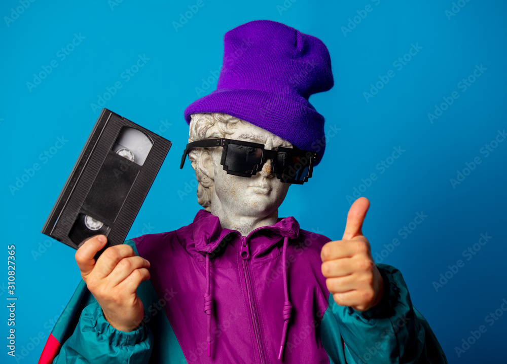 antique statue dressed in trendy clothes of the nineties holds VHS cassette antique statue dressed in trendy clothes of the nineties holds VHS cassette