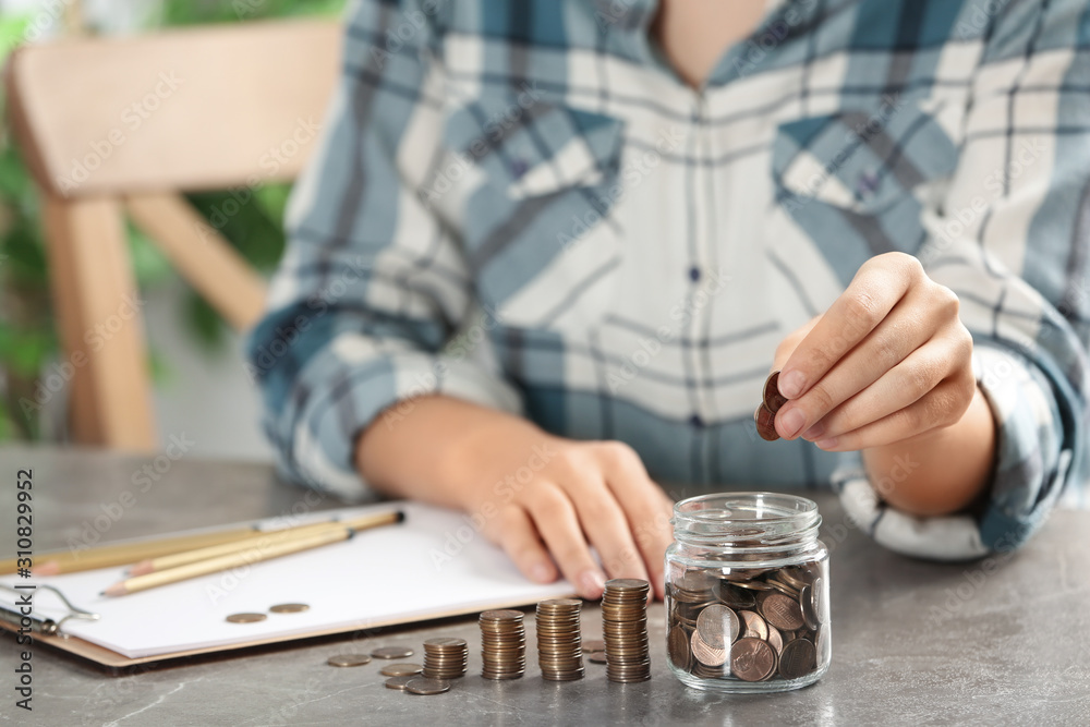Woman putting money into glass jar at table, closeup