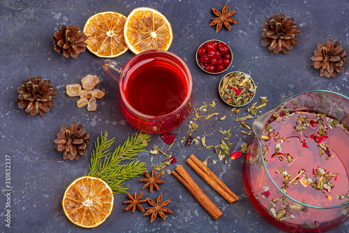 Hot Christmas drink. Red tea (rooibos, hibiscus, karkade) in glass cup and teapot for Christmas feast among cranberries, orange, cones, cinnamon. Winter holidays, new year concept. Close up