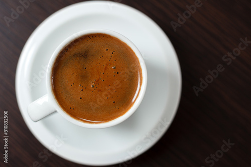 Close-up of single white cup of coffee on dark wooden table. High angle view  flat-lay. Selective focus on coffee surface