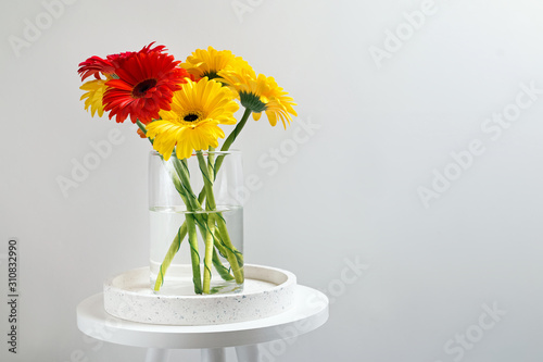 Colorful bunch of gerbera flowers in a glass vase standing near the white wall.