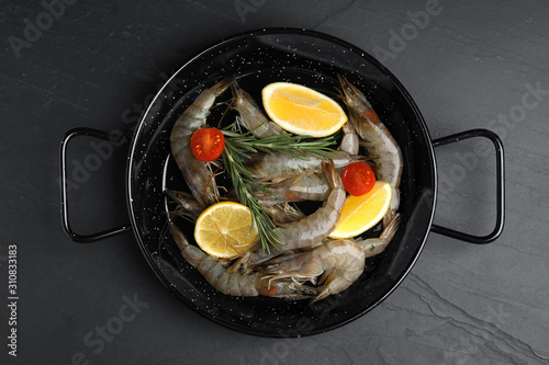 Fresh raw shrimps with lemon slices on black table, top view