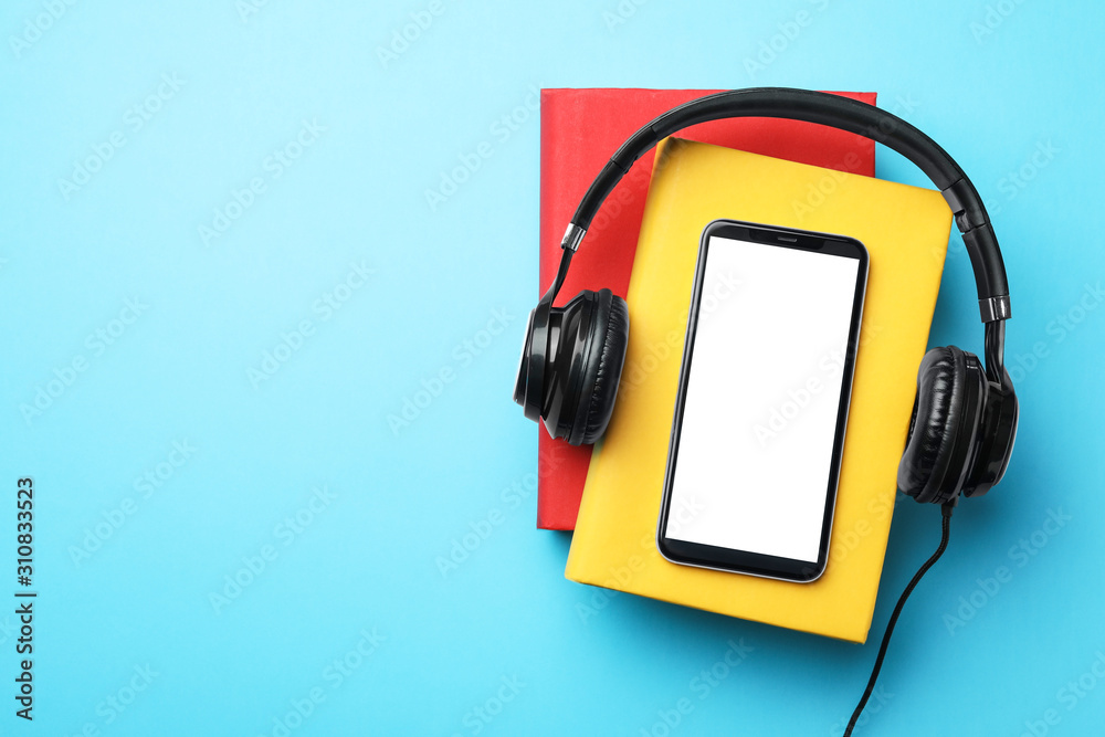 Books with modern headphones and smartphone on light blue background, top view. Space for text Books with modern headphones and smartphone on light blue background, top view. Space for text