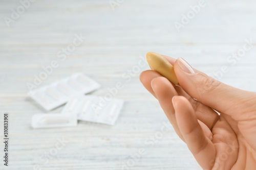 Woman holding suppository at white wooden table, closeup. Hemorrhoid treatment photo