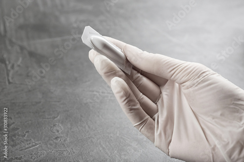 Woman holding suppository at grey table, closeup. Hemorrhoid treatment