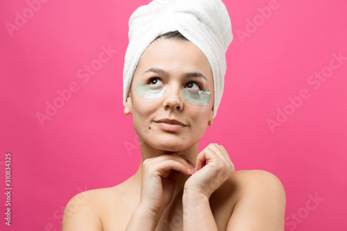 Young beautiful girl in a white towel on his head wears collagen gel patches under her eyes. Mask under eyes treatment face.