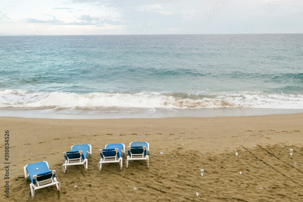 Four empty sun loungers stand on the ocean. plastic trash is scattered around. environmental protection concept Four empty sun loungers stand on the ocean. plastic trash is scattered around. environmental protection concept