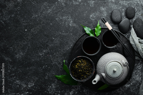 Chinese green tea in a cup with a kettle. On a black stone background. Top view. free space for your text.