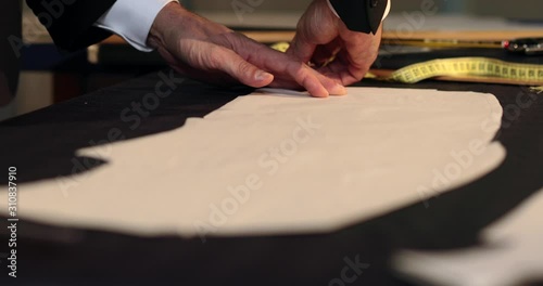 Footage of a tailor drawing lines on fabric and making some alterations arround the cut with his chalk photo