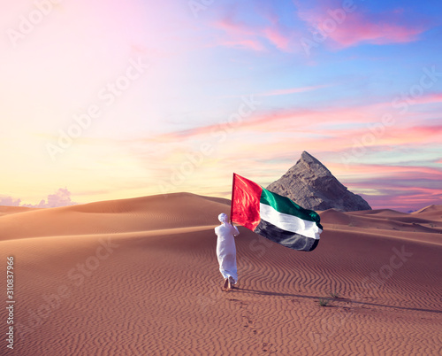 Emirati man holding UAE flag walking in the desert celebrate the national day - spirit of the union