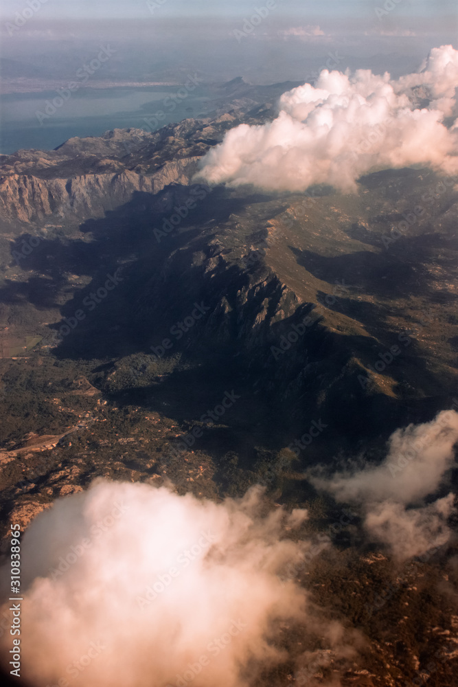 View from airplane window at mountains and pink clouds flying above Montenegro. Aerial perspective. Aerial view of mountain landscape from an airplane window.