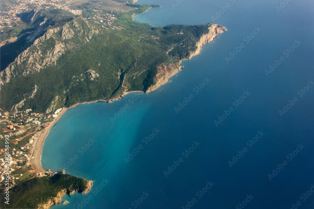 View from airplane window at mountains, seashore and Adriatic sea flying above Montenegro. Aerial perspective. Aerial view of Adriatic coast and seascape from an airplane window.