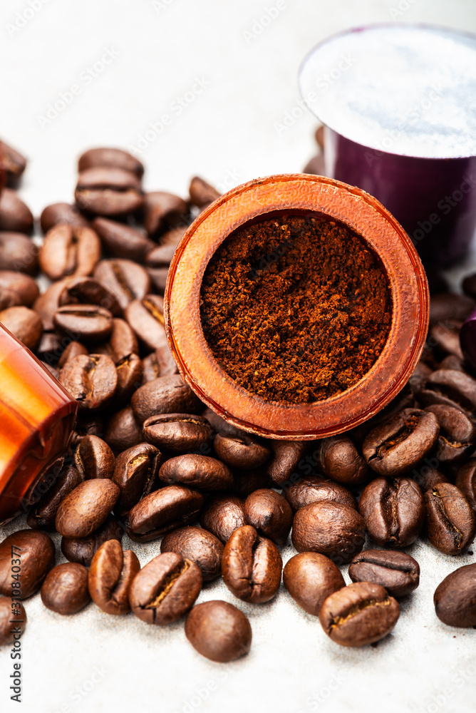 Fototapeta premium Open Espresso coffee capsule with grounded coffee inside, assorted coffee pods and roasted coffee beans on grey background