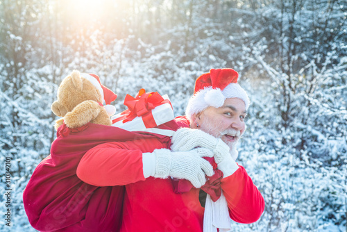 Santa Claus coming to the winter forest with a bag of gifts on snow landscape. Merry Christmas and happy holidays. Santa portrait close up. photo