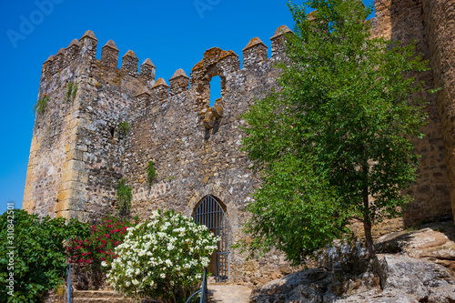 The abandoned stone Aguzaderas Castle in El Coronil, Spain, a ruined 14th century Morrish castle, rests in a field of sunflowers on a cloudless, summer day.