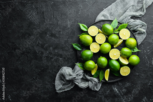 Fresh green limes with leaves. Citrus fruits. On a black stone background. Top view. Free space for your text.