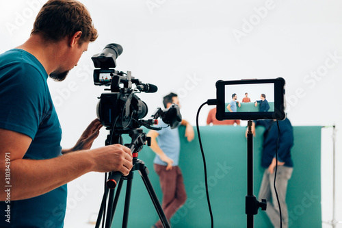 Photo professional camera operator filming video with three actors in the studio