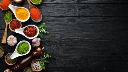 Large spice and herb collection in bowls and spoons. Indian spices. On a black wooden background. Top view.
