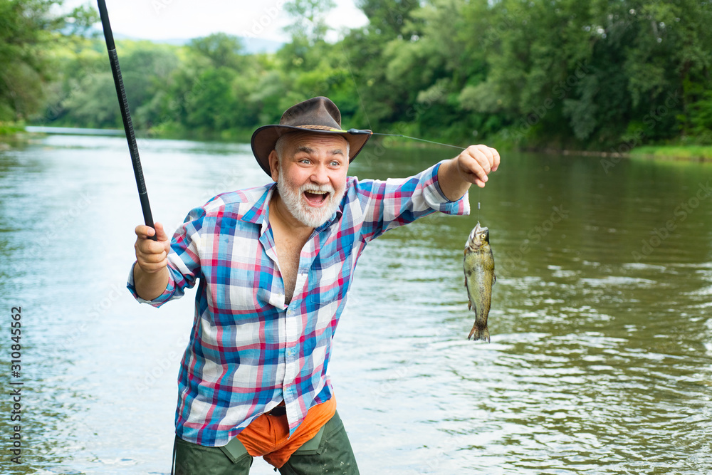 Bearded man catching fish. Male hobby. Against the background of the water  with a reflection of the forest. Retirement is just the beginning. Happy  fly fishing. Just do that only. Photos