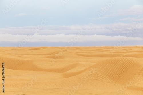 Beautiful deserted landscape of yellow sand of Tunisian Sahara desert and cloudy blue sky. Horizontal color photography.