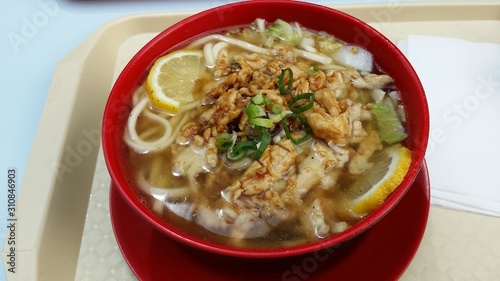 Ramen asian soup with lemon slices and chicken meat in a red bowl and on a white plastic plate. It has slices onion as a topping.