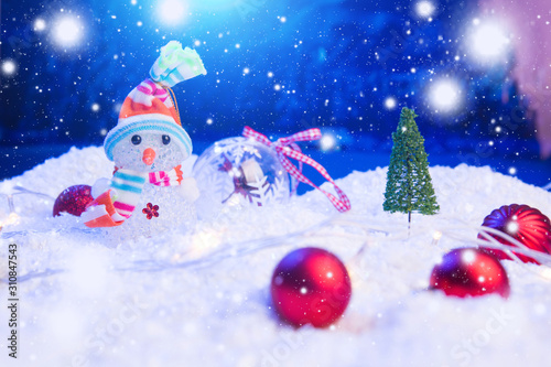 Snow Man with Christmas balls on snow over fir-tree, night sky and moon. Shallow depth of field. Christmas background. Fairy tale. Macro. Artificial magic dreamy world. © Alik Mulikov