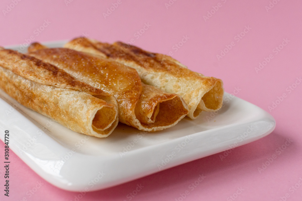 Fried pancakes roll into a tube on a white plate with a pink background. Fried pancakes roll into a tube on a white plate with a pink background.