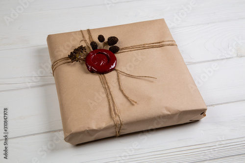 Gift wrapped in craft paper, tied with string and glued wax seal. Lying on the white wooden table