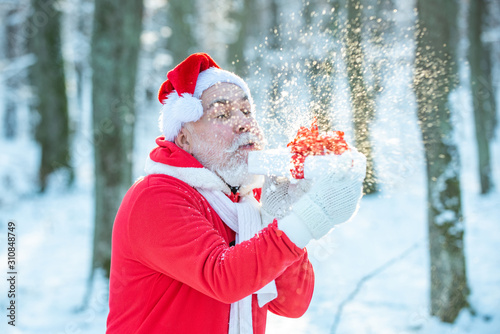 Santa blowing snow - funny face. Santa Claus coming to the winter forest with a bag of gifts on snow landscape. Santa in the winter field. photo