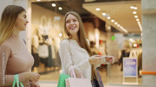 Tracking slow motion zoom in shot of two beautiful young women with shopping bags walking in mall and talking cheerfully