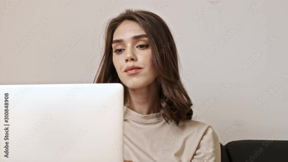 Thoughtful brunette woman using laptop computer while sitting on sofa indoors Thoughtful brunette woman using laptop computer while sitting on sofa indoors
