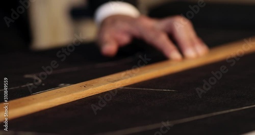 Close up footage of a tailor drawing lines on fabric and making some alterations arround the cut with his chalk photo