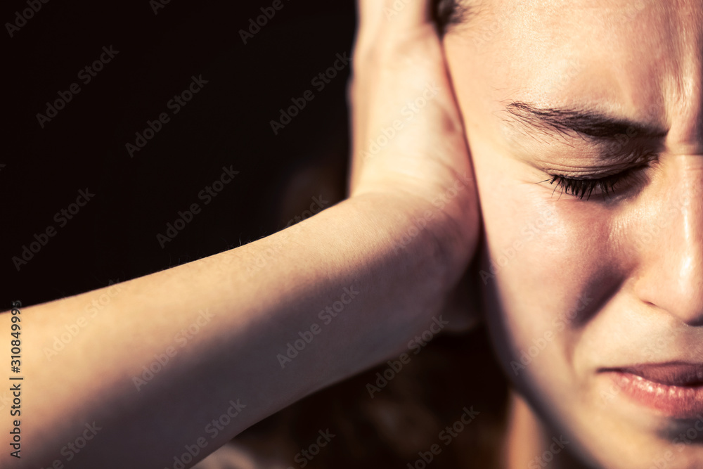 A young woman close-up with headache on black background. Mental illness concept.