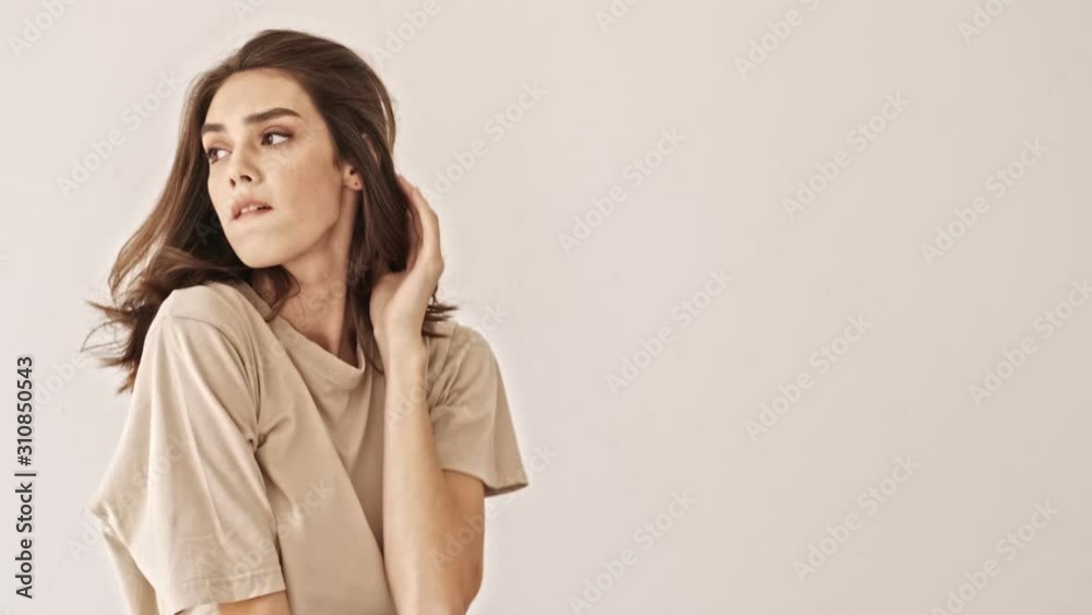 Serious beauty brunette woman playing with her hair and looking around over grey background Serious beauty brunette woman playing with her hair and looking around over grey background